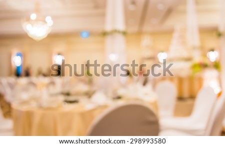 blurred image of Large dining table set for wedding, dinner or festival event with beautiful lights decoration inside large hall with people.