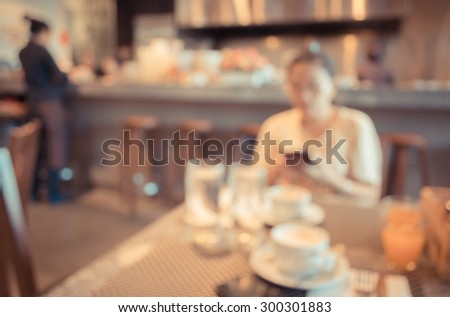 blur image of woman use mobile phone in coffee shop for background usage(vintage color tone)