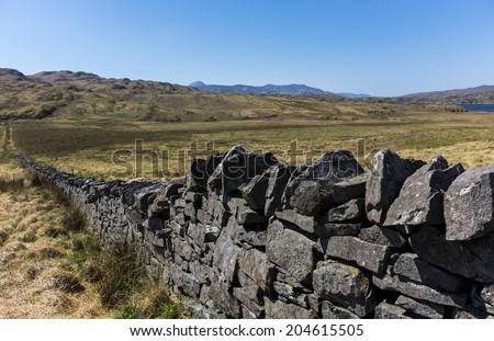 Dry stone wall in remote rural setting on the Hebridean island of Jura, Scotland, with view over grassland and hills to Islay.