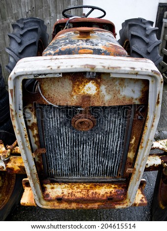 Obsolete farm tractor in closeup front view over water radiator, showing details of rust and decay.
