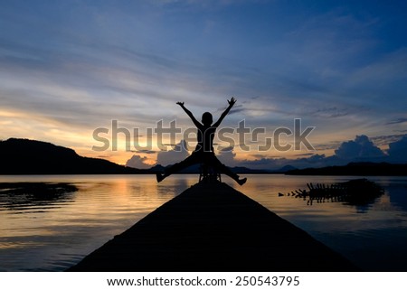 An excited silhouetted kid jumping spreading his arms and legs on a bridge with a sunset background