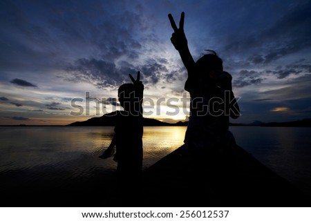 Silhouetted kids. Siblings enjoying sunset, the sister showing peace hand sign looks very excited and happy while drinking an energy/soft drink while the younger brother joins the enjoyment