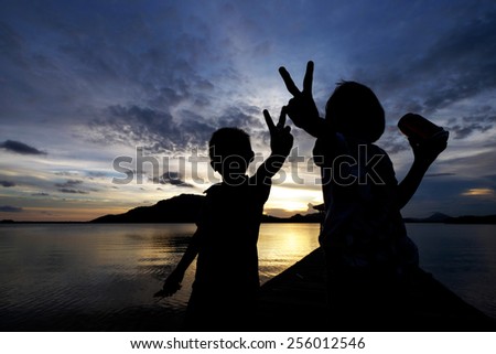 Silhouetted kids (Excited and joyous sibling,both sister and younger brother showing peace hand sign, while the sister enjoying her energy drink) during sunset