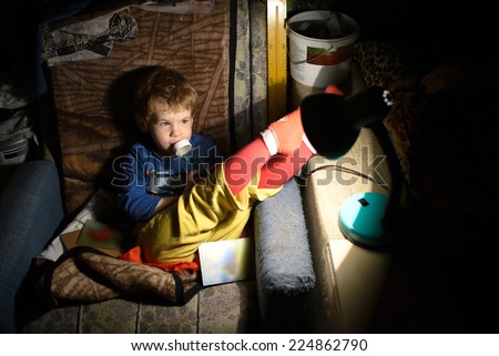 Child Eats. Child Sitting On a Chair In a Dark Room In Front Of The Lamp And Eats