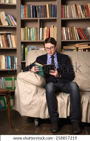 Old-fashioned Young man is sitting in a library and reading a book.