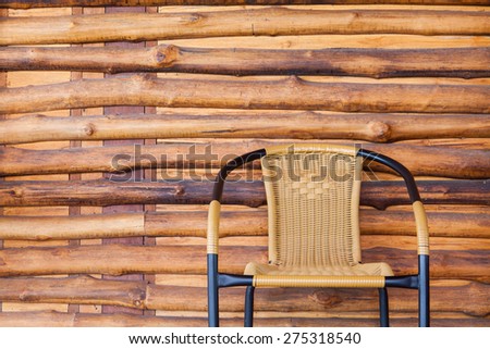 Black steel frame chair with woven rattan blend stripes. Placed in front of the house where the walls are adorned with brown slab.