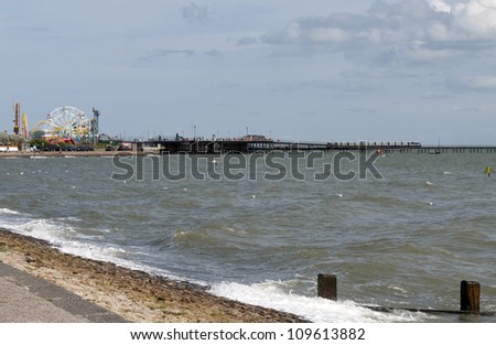 August 2012. Southend Pier with its fun fare including big wheel and a railway to take you to the end. Longest pier in England seen on a  summer day with choppy waves breaking against the pebble beach