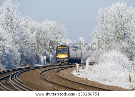 Passenger train with its yellow front set against the hoar frost on the trees and bushes as it Approaching March, Cambridgeshire on a cold and frosty morning.