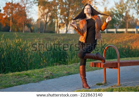 Full figure glamourous portrait of the young beautiful woman in leather boots in the park