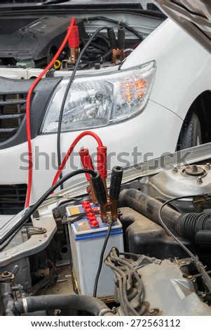 Using jumper cables to charge a dead car battery from  another vehicle in raining day.