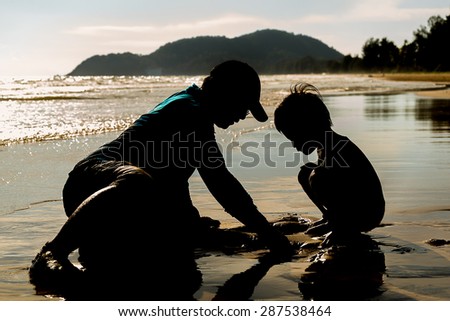 Silhouettes of Father and two boys  playing on the beach in Warm tone