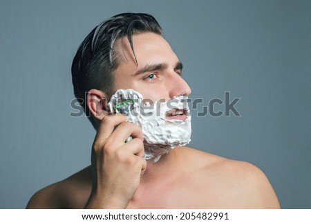 Young man shaving with razor and foam