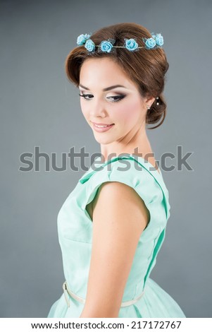 Young beautiful brunette in green dress and flowers on her head posing on grey background