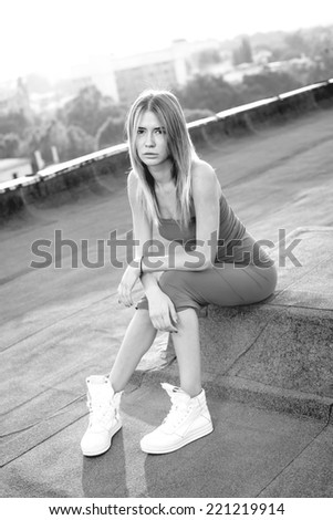 Beautiful young woman wearing a purple dress with a pair of white sneakers on the roof. Sunset