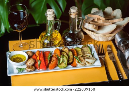 Grilled vegetables on yellow and black background with a glass of wine, oil, vinegar and bread.