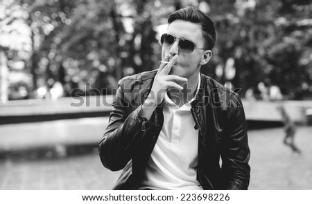 A handsome man with sunglasses in a leather jacket on the street smoking
