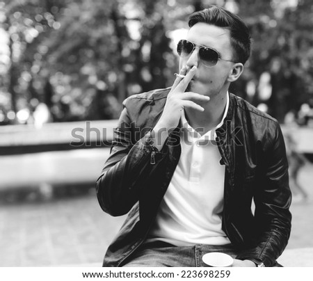 A handsome man with sunglasses in a leather jacket on the street smoking