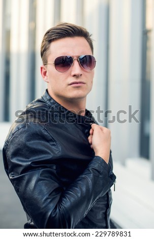 Young, fashioned man in black leather jacket, sunglasses and jeans. Outdoor portrait