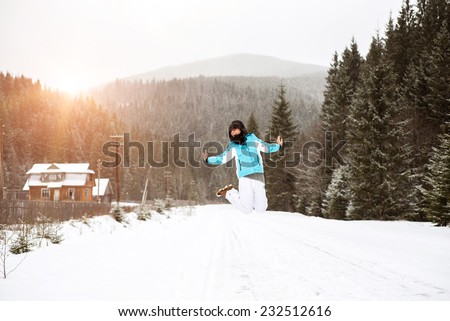 Happy girl jumping up in the mountains on the road that people have gone over. Scene is covered in snow on the sunset.