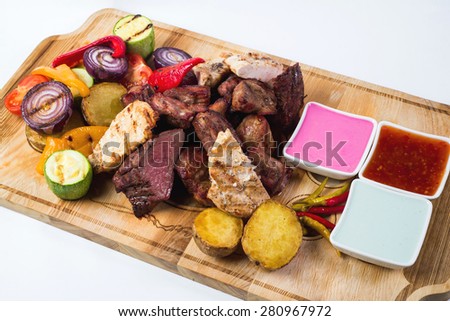 Different kind of grilled meat with sauces on wooden plate isolated on white background.