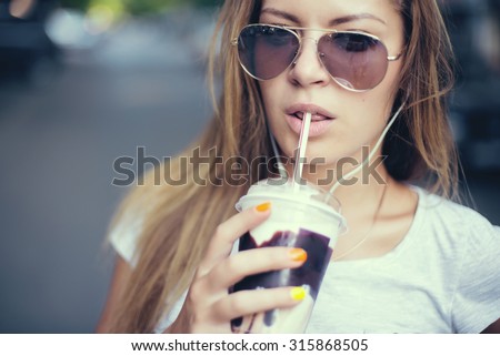 pretty girl with milk shake listening music on the street. Sunset