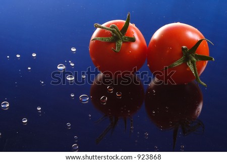 Tomatoes and water droplets on reflective blue base.