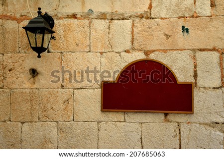 Ancient wall with old-fashioned streetlamp and vintage looking empty red plate