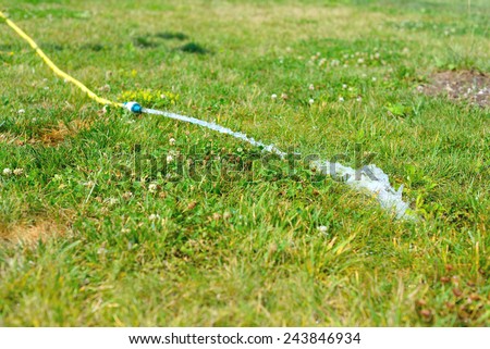 Yellow rubber hose on a grass with water flowing from it