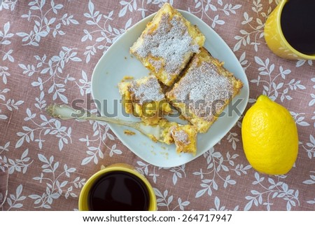 Lemon tarts powdered with sugar, yellow mug with tea and lemon f