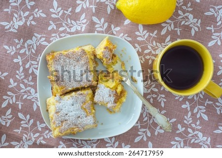 Lemon tarts powdered with sugar, yellow mug with tea and lemon f