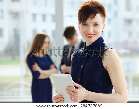 Business woman standing in foreground and her co-workers discussing business matters in the background