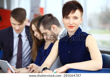 Smiling business woman in foreground  and her co-workers discussing business matters in the background