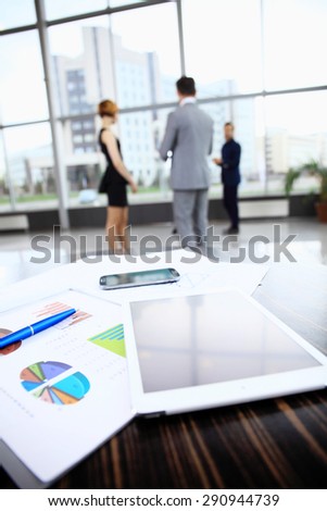 Business background with business people and table with graphics, telephone and tablet computer in foreground