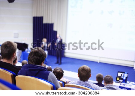 Business man is making a speech in front of a big audience at a conference hall.