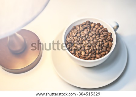 a Cup of coffee grain bean caffeine candlestick table lamp wooden background selective soft focus