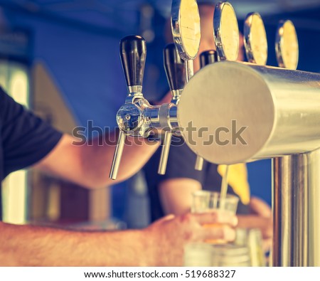Barman hand at beer tap pouring a drought lager beer serving in a restaurant or pub.Vintage look