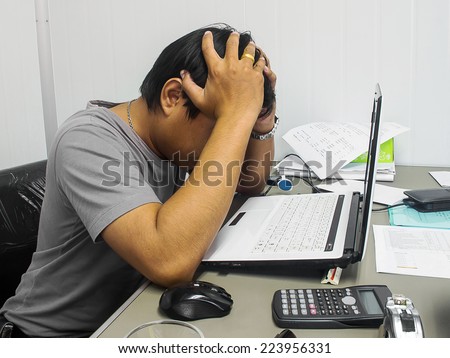 Tired or depressed businessman sitting at he desk behind he laptop with he hands covering he eyes