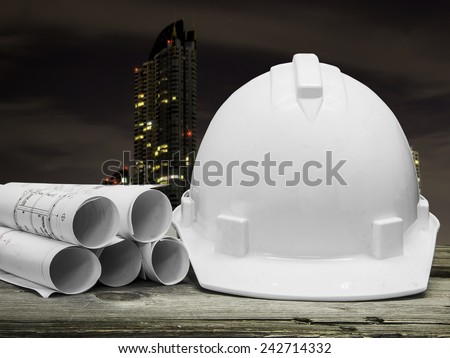 Safety helmet with architectural blueprint of office building over Construction site background