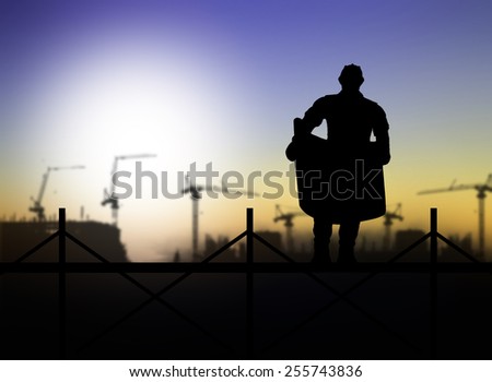 silhouette of engineer looking at blueprints on scaffold in a building site over Blurred construction site
