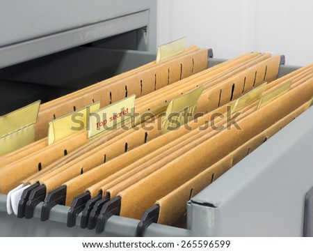 Abstract background image of colorful hanging file folders in drawer with top secret stamp . Macro with with extremely shallow dof. Selective focus in front edges of files.