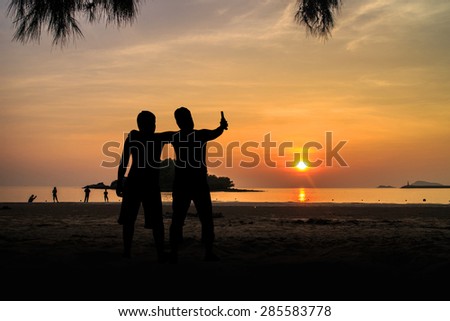 Silhouette Two young men on the beach having party, drinking and having a lot of fun in the sunset