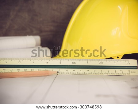 Pencil on architectural blueprint of office building over blurred Safety yellow hat and blueprint