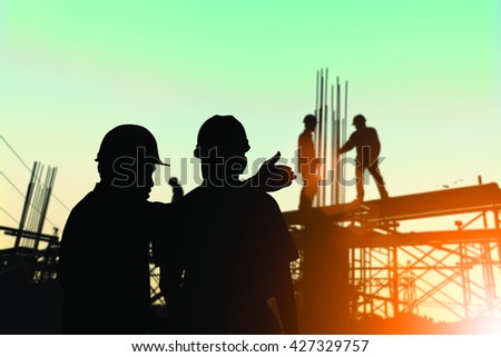 Silhouette engineer standing orders for construction crews to work safely on high ground over blurred construction workers natural background sunset pastel. heavy industry and safety at work concept.