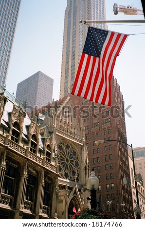 A church and high houses in the city of Chicago with the American flag in the foreground
