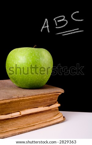 Green apple on top of a very old book. Chalkboard with “ABC” letters on it as background