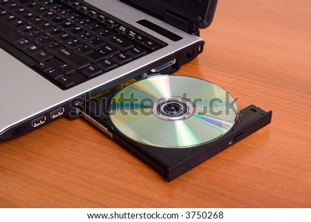 Partial view of a laptop with the dvd recorder opened on a wood table