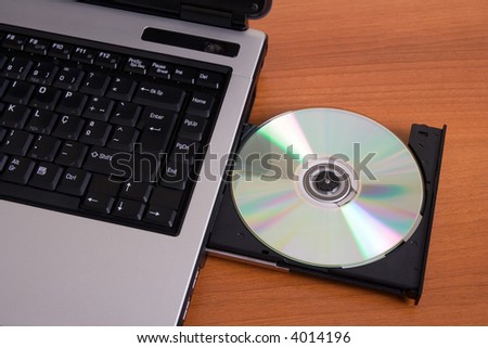 Partial top view of a laptop with the dvd recorder opened on a wood table