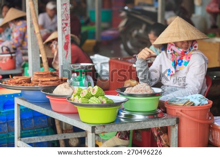 VIETNAM - DECEMBER 2014: Traditional asian market saleswoman in conical hat sits at the stall with local dishes
