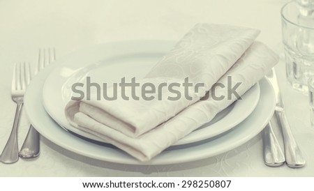 White dining table serving. White napkins, plates. forks, knifes