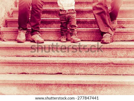 Legs in blue jeans and hiking shoes - Happy family  with two-year-old child walking down old stairs - dark red tinted black and white vintage effect